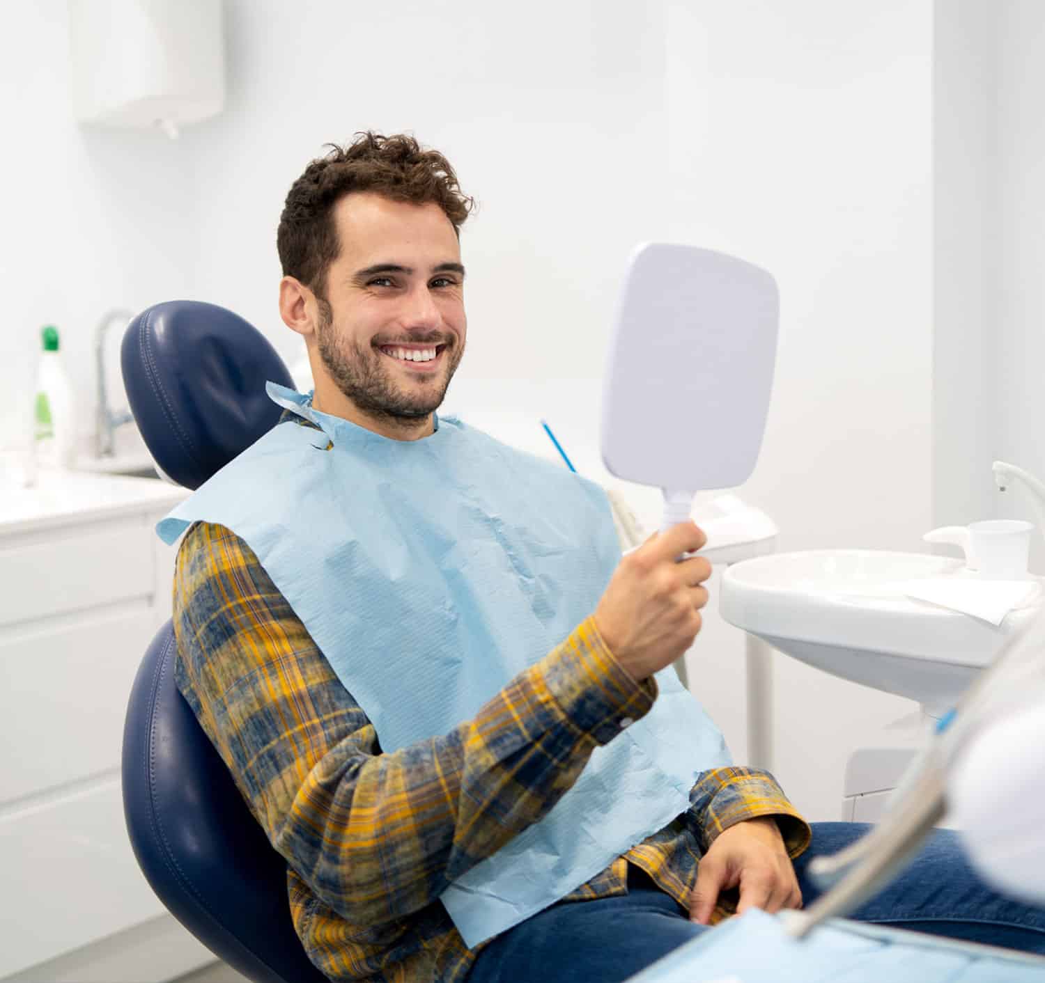 Happy male patient looking in hand mirror at the dentists