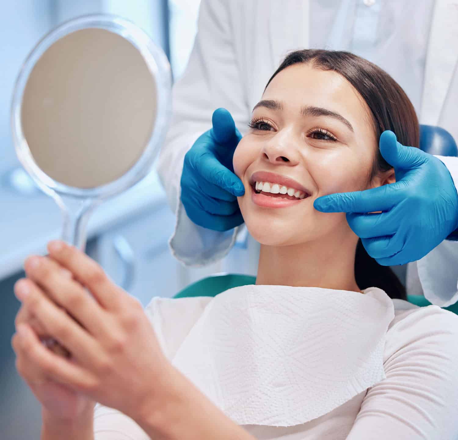 Happy female patient looking at her teeth in hand mirror at the dentists